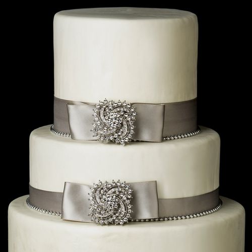 Two-tiered wedding cake with silver ribbons and decorative elements on a black background